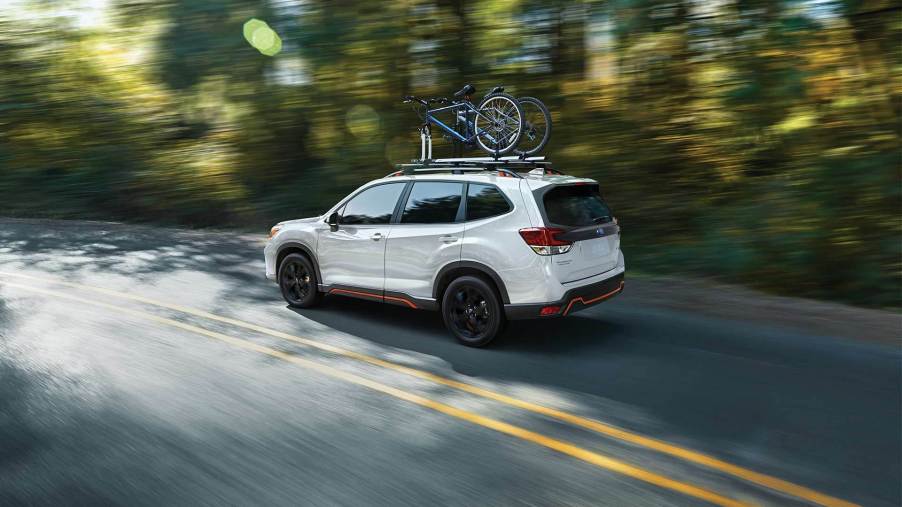 A white 2021 Subaru Forester driving down a tree-lined road.