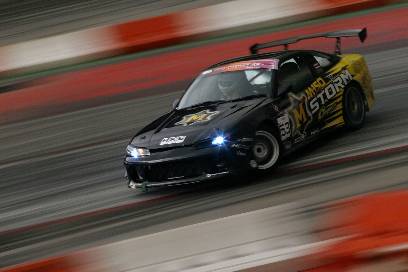 A Nissan S14 drift car siding on track with its headlights on.