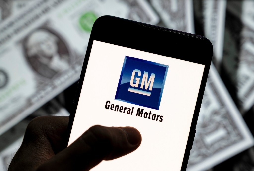 The General Motors (GM) logo displayed on a smartphone with U.S. dollars in the background