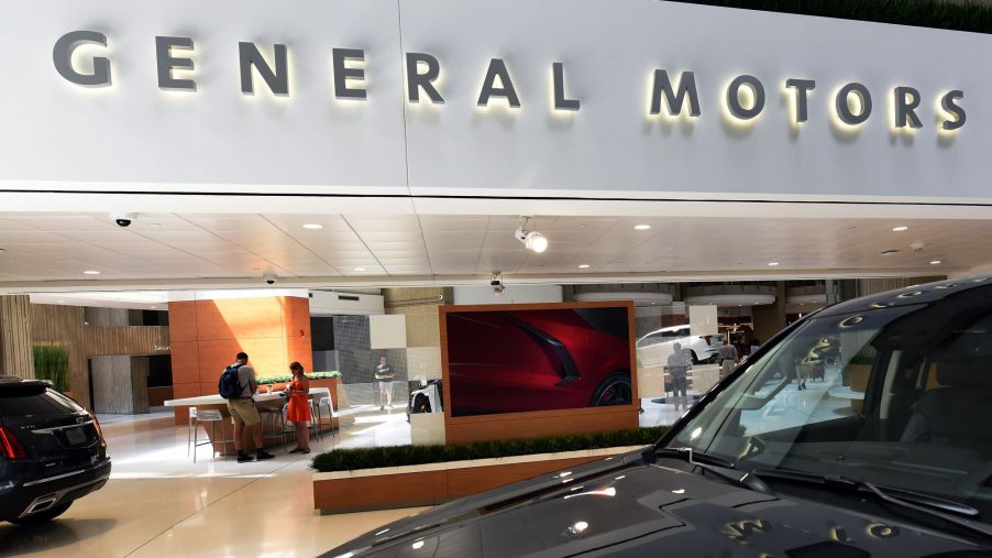 A General Motors (GM) sign inside of a building with cars and office furniture.