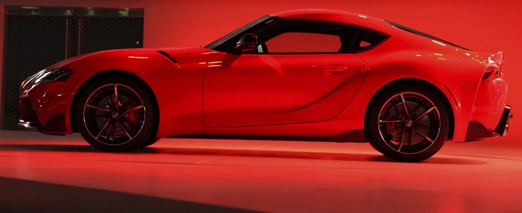 A brand new 2020 Supra at an auto show, bathed in red overhead light shot in profile