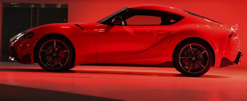 A brand new 2020 Supra at an auto show, bathed in red overhead light shot in profile