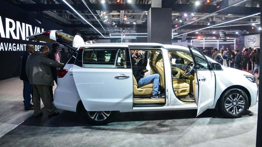 the 2022 kia carnival on display at an indoor auto show with onlookers testing the seats and viewing the exterior