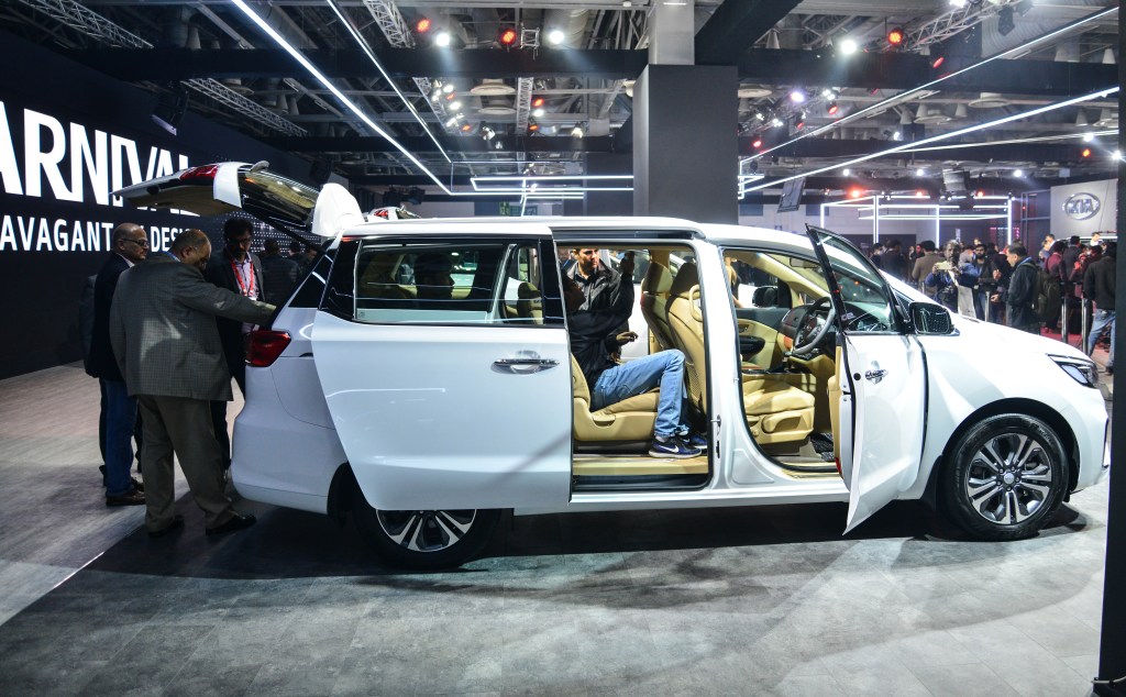 the 2022 kia carnival on display at an indoor auto show with onlookers testing the seats and viewing the exterior