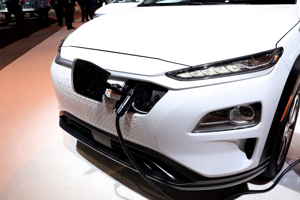 A white Kona EV charging at an auto show