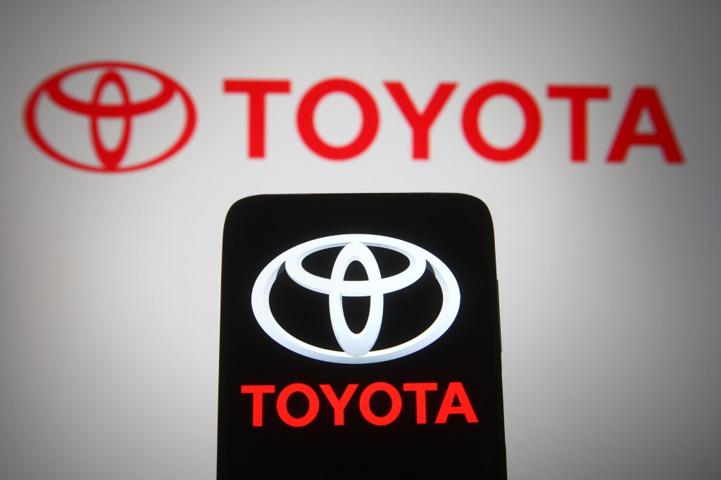 A red Toyota Logo on a computer screen with a smartphone in front of the screen also displaying the logo.