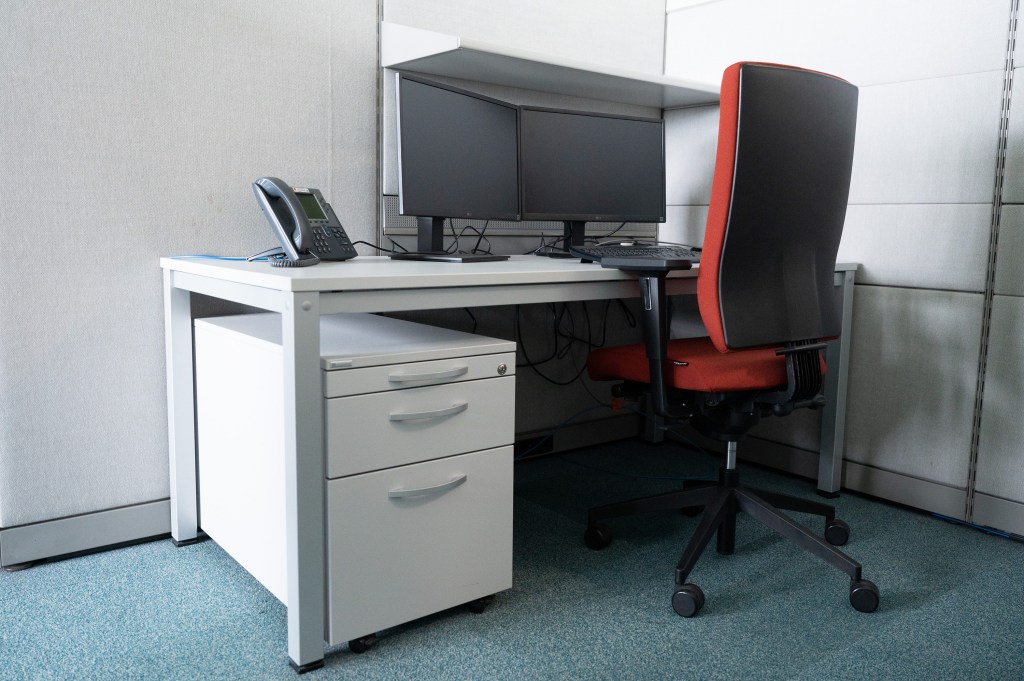 An empty cubicle with two computer monitors and a red chair