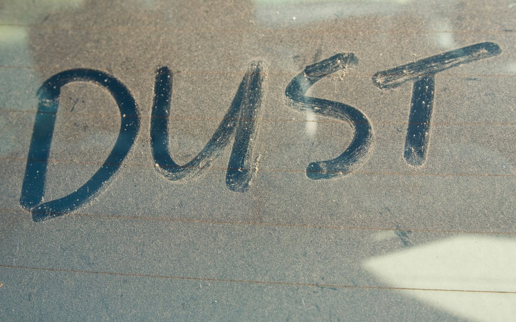 the word dust spelled out by rubbing a finger on a dirty windshield 
