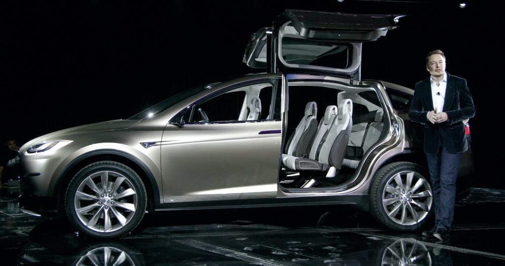 A gray Tesla Model X and Elon Musk at a press event. The Model X is among the best electric SUVs of 2021.