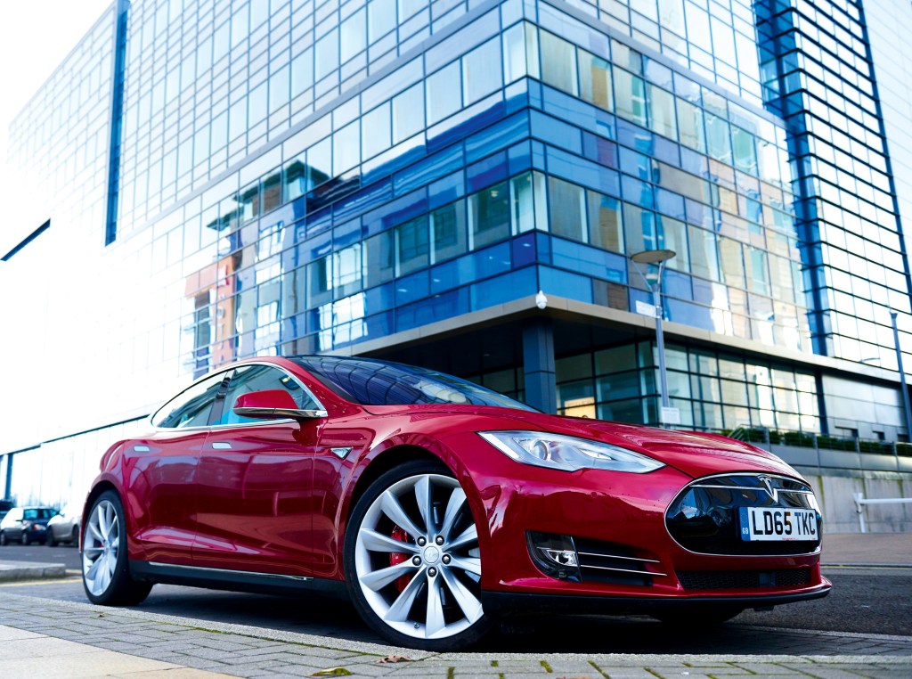 A Tesla Model S sedan parked streetside under a building