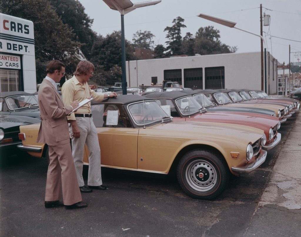A second hand car salesman and a man admiring brand new Triumph TR2s in the UK. Photo by Lambert/Getty Images. Do open recalls change a cars trade-in value.