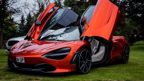a red McLaren 720S with the doors open parked on the grass