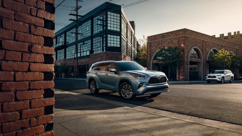 A silver 2021 Toyota Highlander driving down a street surrounded by brick buildings.