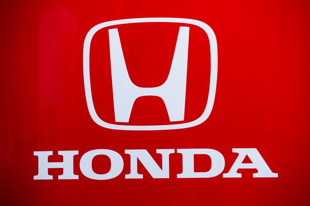A white Honda logo with Honda written underneath on a red background. 