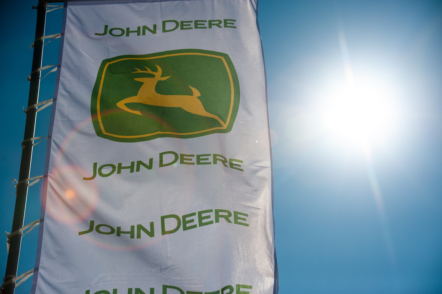 The John Deere logo on a white flag with the sun shining through it, Consumer Reports recommends several of the best John Deere zero-turn mowers
