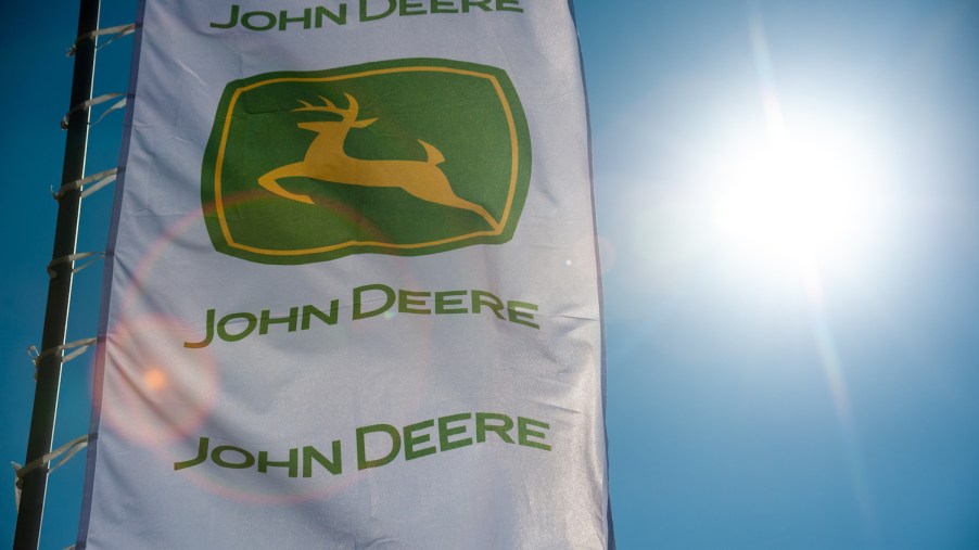 The John Deere logo on a white flag with the sun shining through it, Consumer Reports recommends several of the best John Deere zero-turn mowers