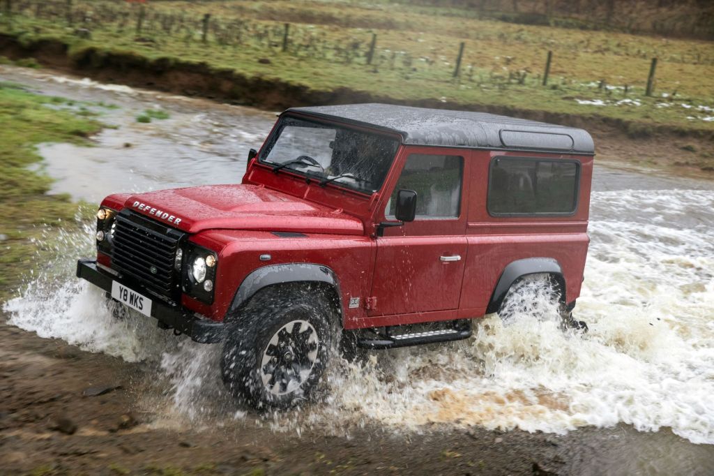 A Land Rover Defender V8 Heritage model driving through a shallow river