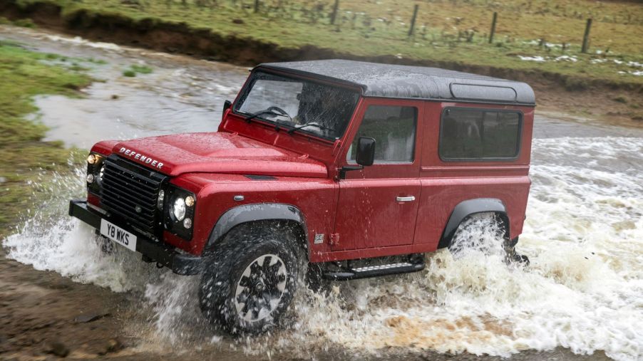 A Land Rover Defender V8 Heritage model driving through a shallow river