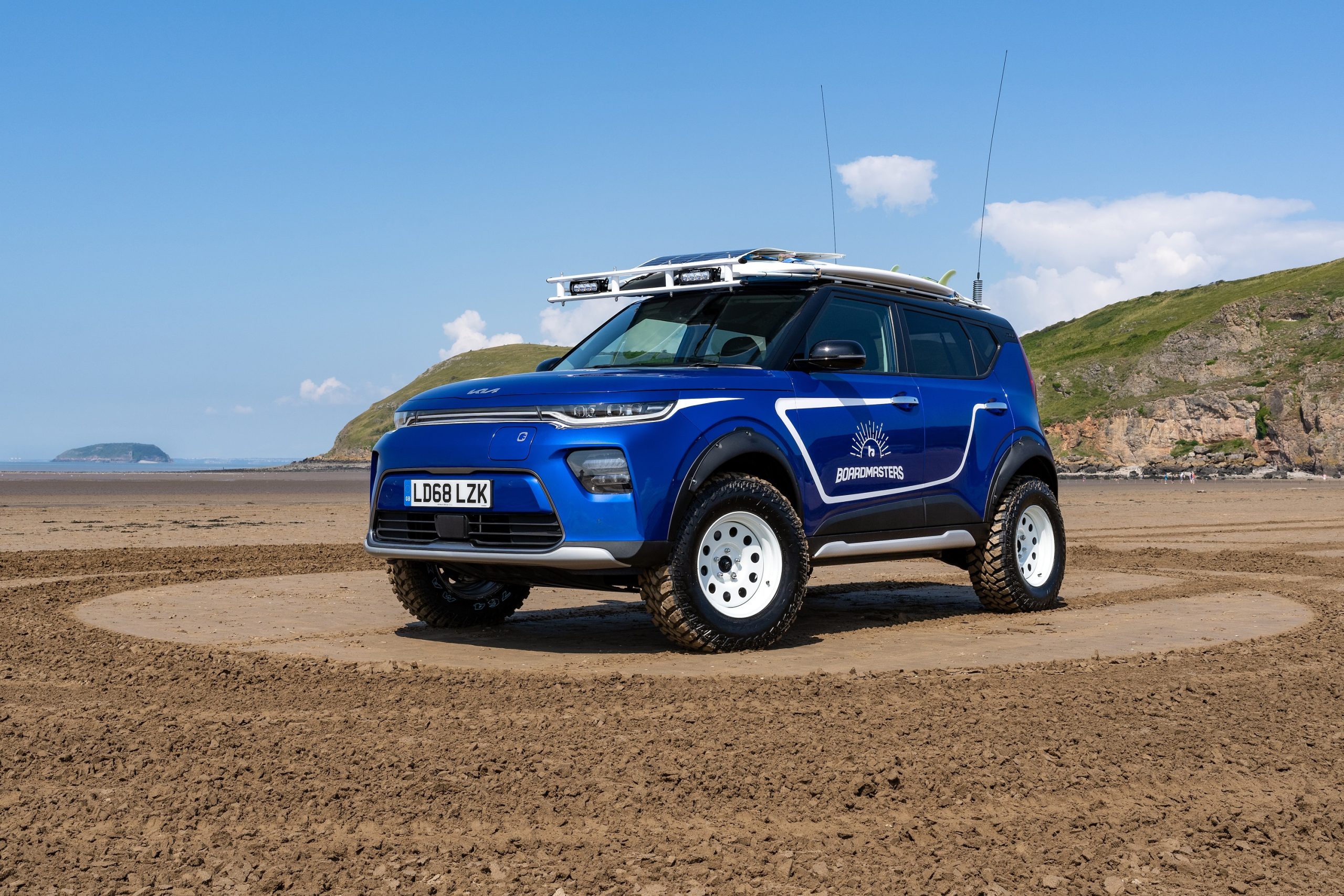 The lifted, blue Kia Beach EV with surfboards mounted on the roof
