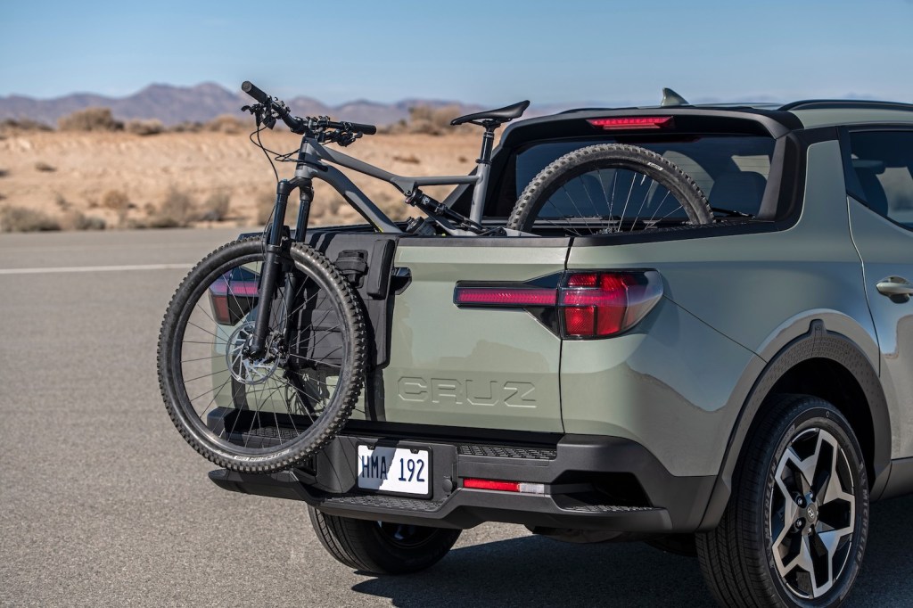 This is a promotional photo of a light green Hyundai Santa Cruz with a bicycle in its truck bed. The Santa Cruz is a crossover truck with the smallest truck bed available.