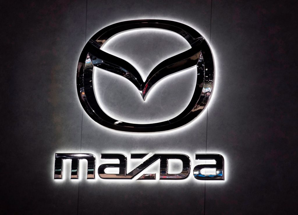 An illuminated chrome Mazda sign with Mazda written underneath the logo on black background.