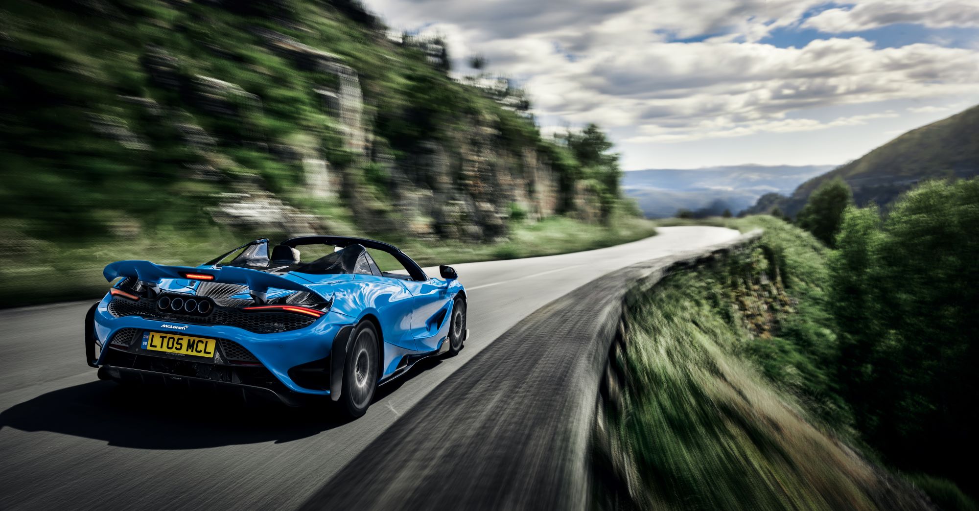 The McLaren 765LT Spider in blue driving down a country highway near cliffs