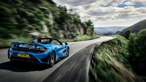 The McLaren 765LT Spider in blue driving down a country highway near cliffs