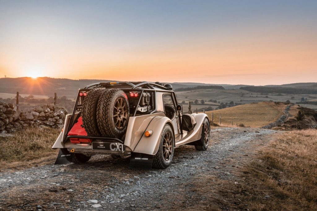 The rear 3/4 view of a tan Morgan Plus Four CX-T on a rocky plains trail