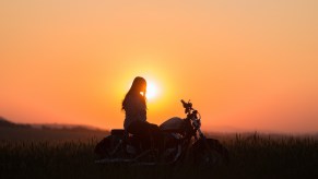 Woman watches the sunset from a motorcycle in the Adirondack mountains.