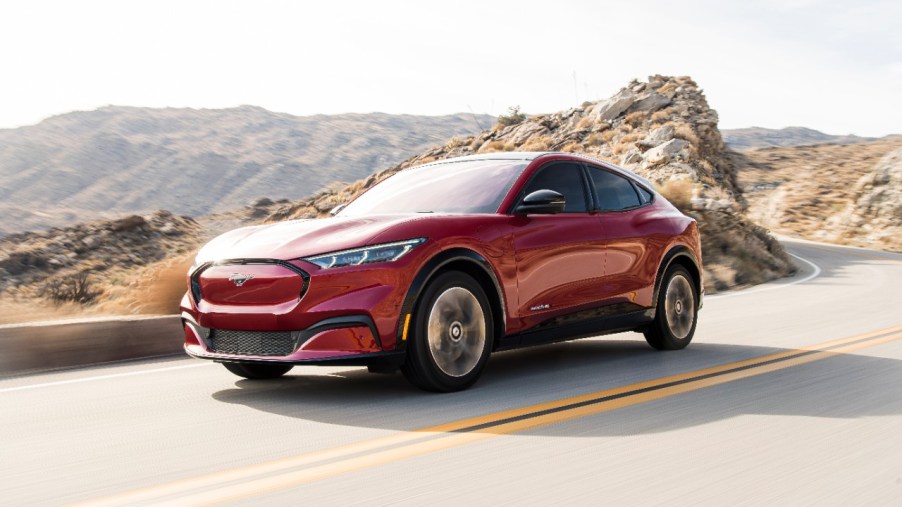 A red 2021 Ford Mustang Mach-E driving, the Mach-E is an electric SUV in direct competition with the Tesla Model Y