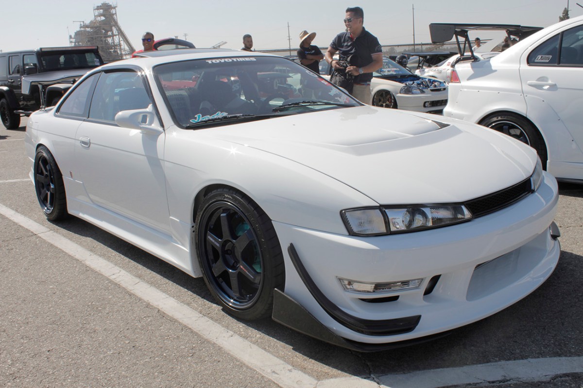 A white 1998 Nissan 240SX with blue wheels and a body kit. One of the great Japanese sports cars.