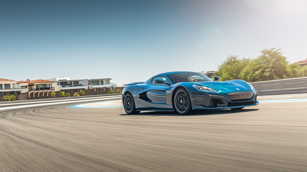 A turquoise-blue Rimac Nevera electric supercar driving on a track on a sunny day