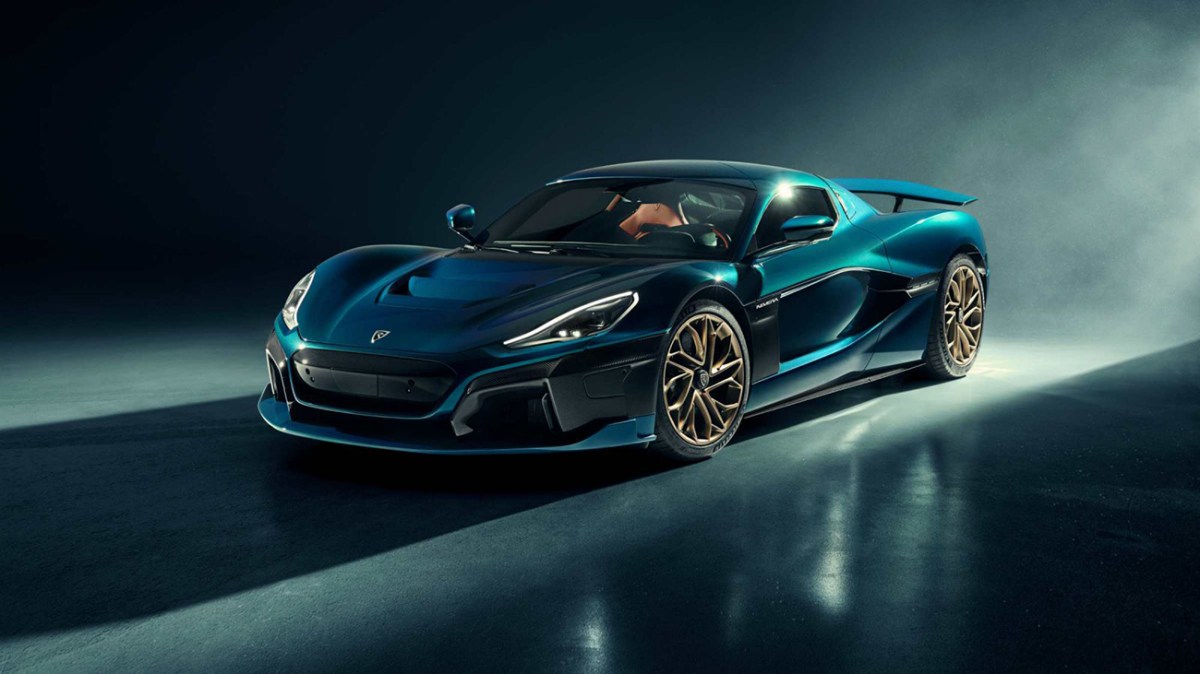 A blue Rimac Automobili Nevera electric super car in a dark studio room with light shining down from the back.