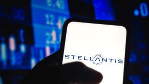 The Stellantis logo on a smartphone with a background of numbers and prices