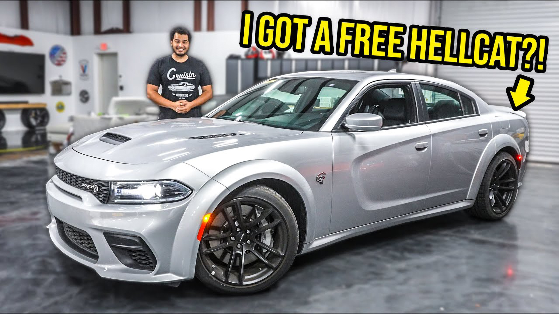 YouTuber "Tavarsh" standing next to a silver Dodge Charger Hellcat Redeye.