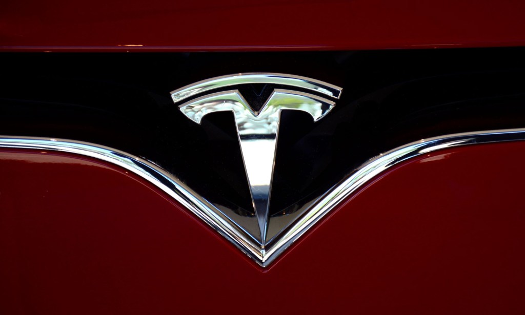 A chrome Tesla logo on a black background on a red car.