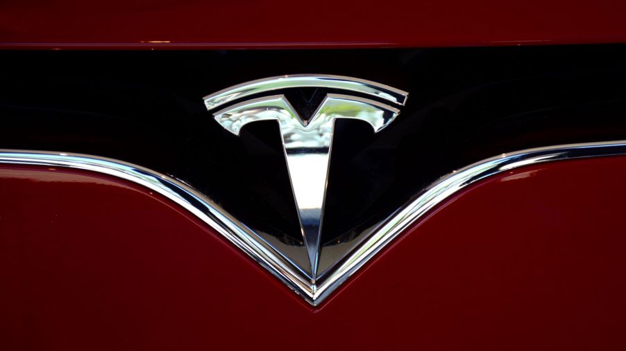 A chrome Tesla logo on a black background on a red car.