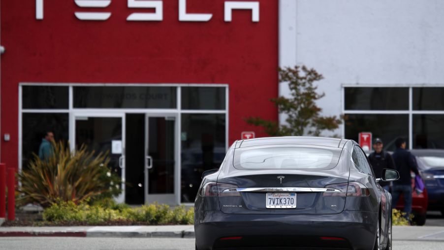 A Tesla Model S driving to a parking lot outside of a Tesla showroom