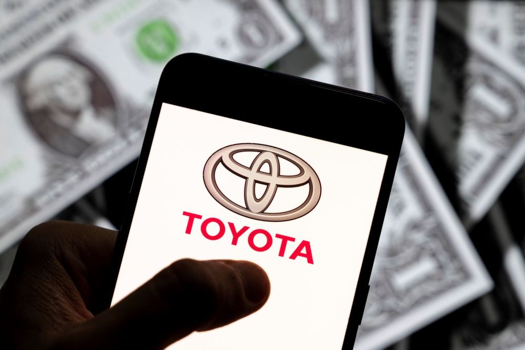 The affordable car Toyota logo on a smart phone with dollar bills in the background.