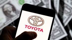 The affordable car Toyota logo on a smart phone with dollar bills in the background.