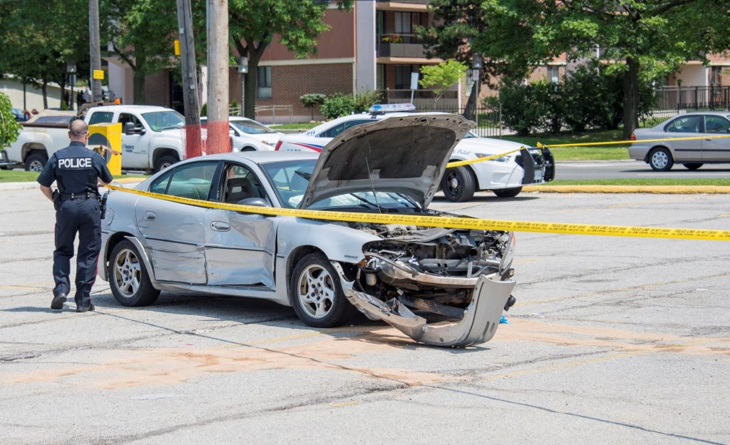 A police officer standing next to a totaled vehicle surrounded by police tape