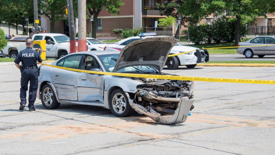 A police officer standing next to a totaled vehicle surrounded by police tape