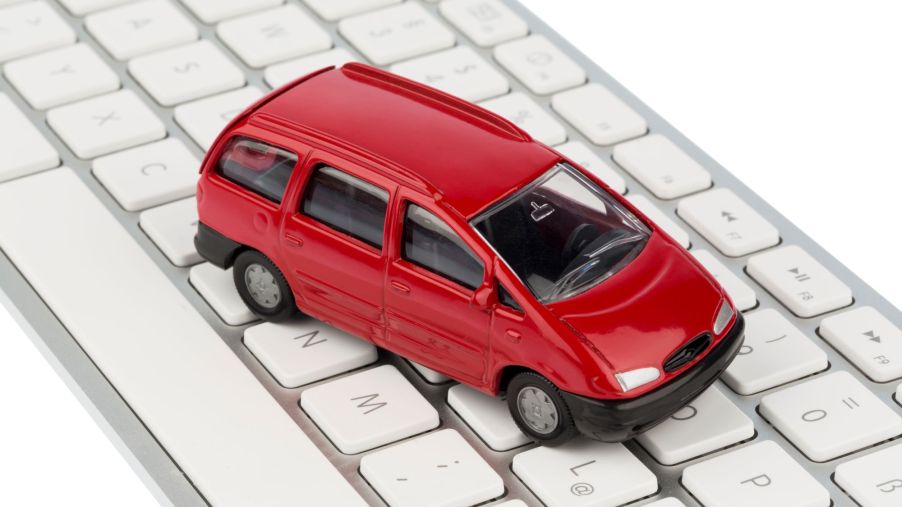 A tiny red minivan toy placed on top of an Apple keyboard
