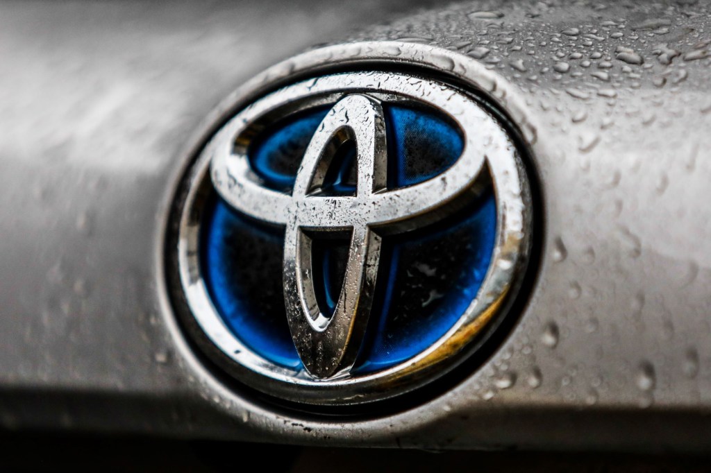 A chrome Toyota logo with a blue center on a silver car with water drops.