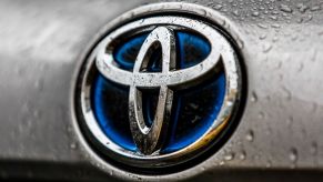 A chrome Toyota logo with a blue center on a silver car with water drops.