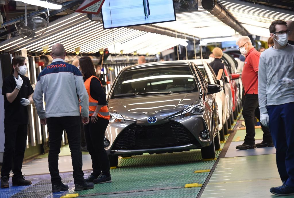 Toyota Manufacturing plant with people standing around assembling cars with multiple cars coming down the line.