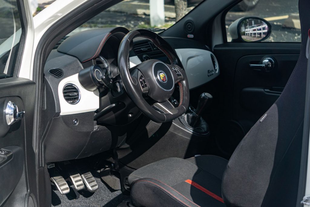 The black-and-red seats and white dashboard of a white used 2013 Fiat 500 Abarth
