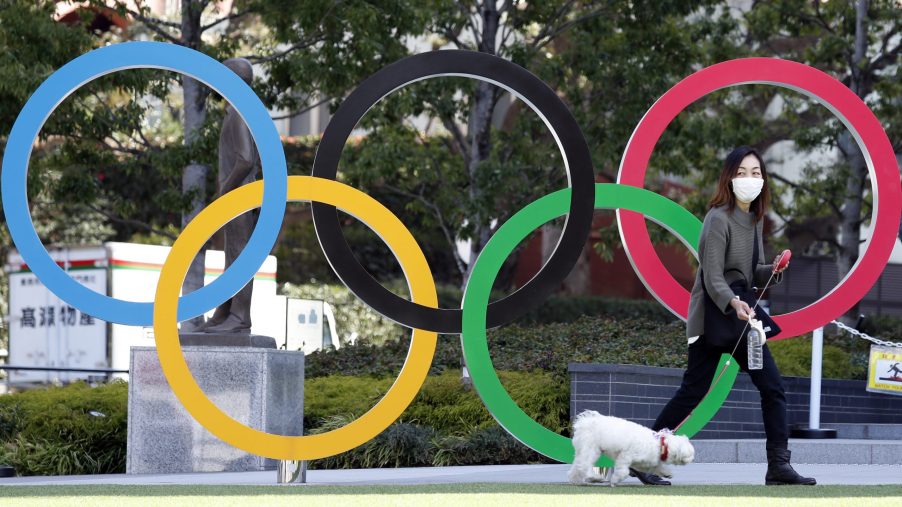 A woman wearing mask walks her pet dog past the Olympic rings
