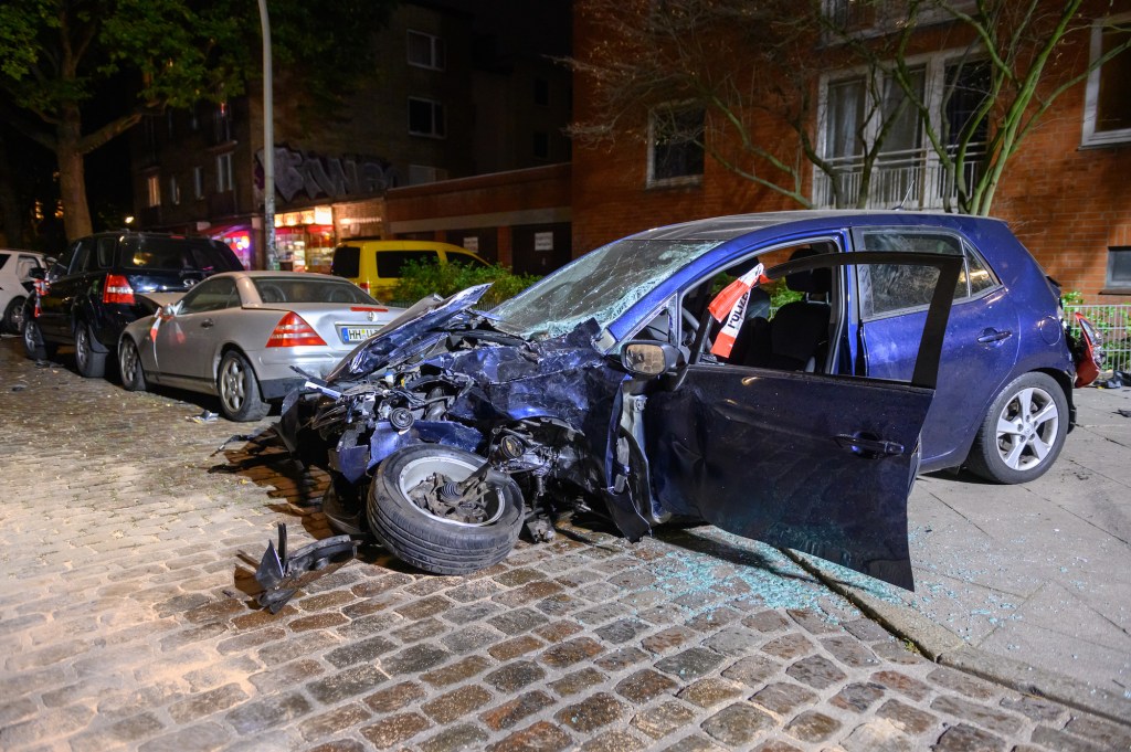 Damaged and destroyed vehicles are parked at the cordoned-off accident site in the residential street.