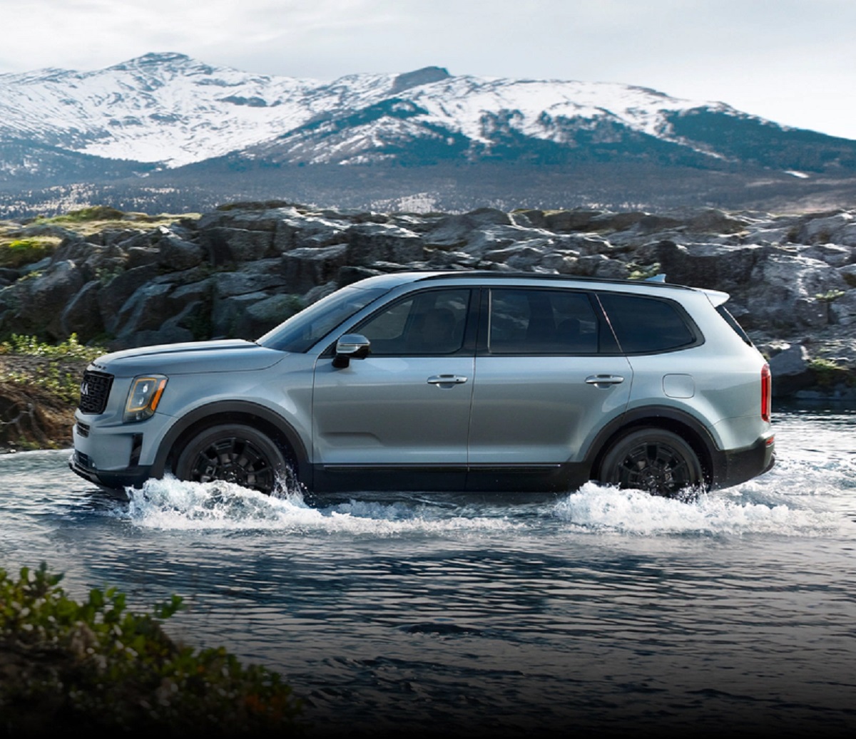 A silver 2021 Kia Telluride splashing through a river with a mountain in the background.